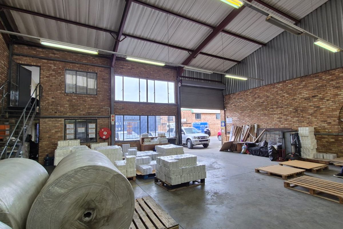 Spacious industrial warehouse unit featuring exposed brick walls, high-clearance metal roofing, concrete flooring, and a large roller shutter door for easy access.