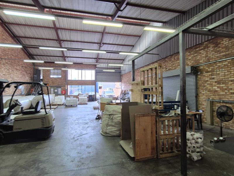 Spacious industrial warehouse unit featuring exposed brick walls, high steel truss ceilings, concrete flooring, and a large roller shutter door for easy access.