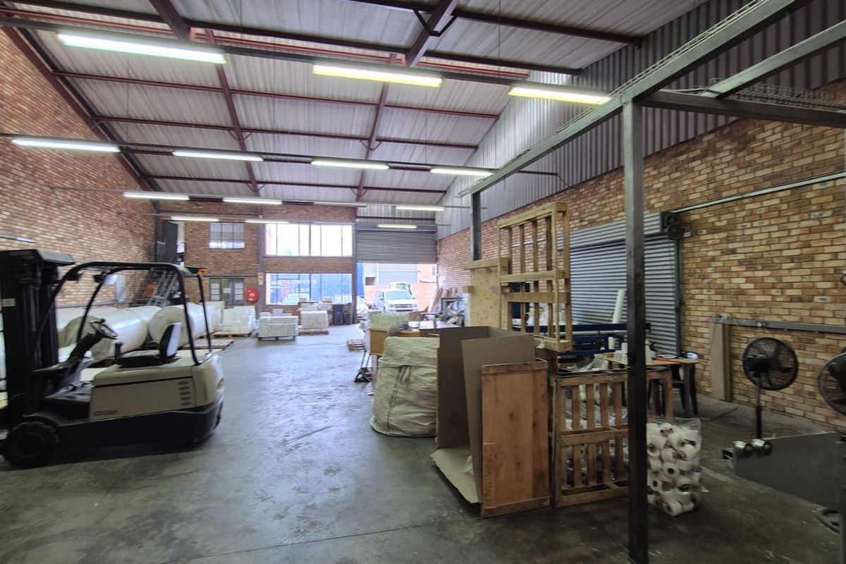 Spacious industrial warehouse unit featuring exposed brick walls, high steel truss ceilings, concrete flooring, and a large roller shutter door for easy access.