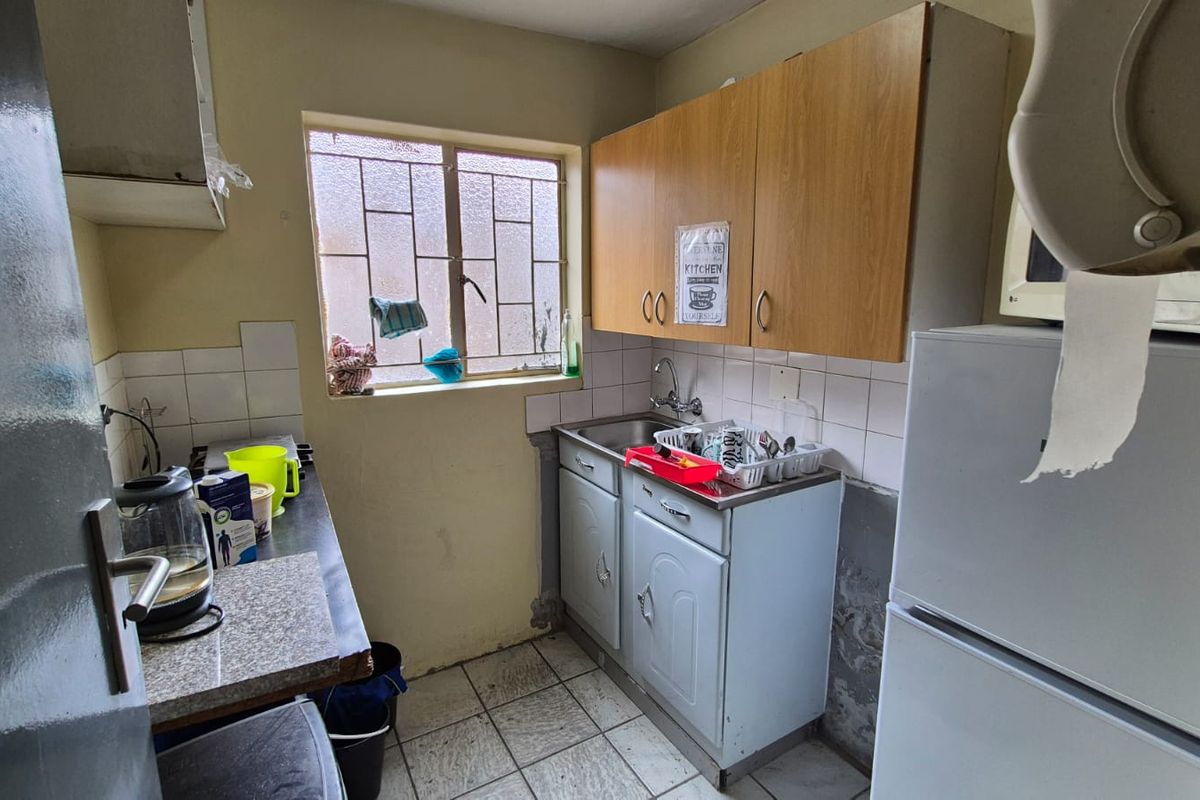 Compact kitchen featuring built-in cabinetry, a stainless steel sink, tiled backsplash, and tiled flooring, requiring cosmetic updates to improve its overall condition.