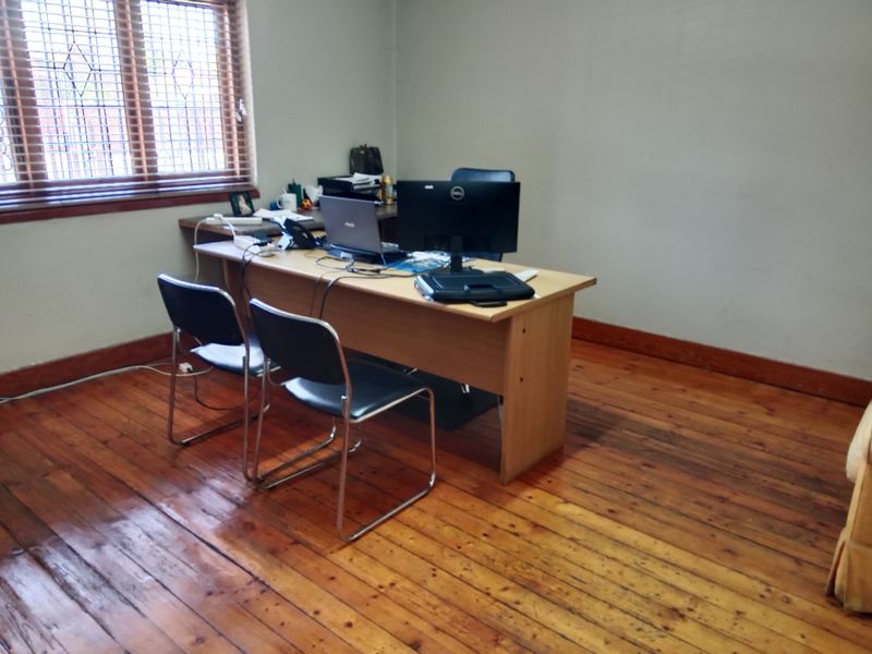 A functional office space featuring polished timber flooring and a large window with venetian blinds, providing natural light for a workspace.