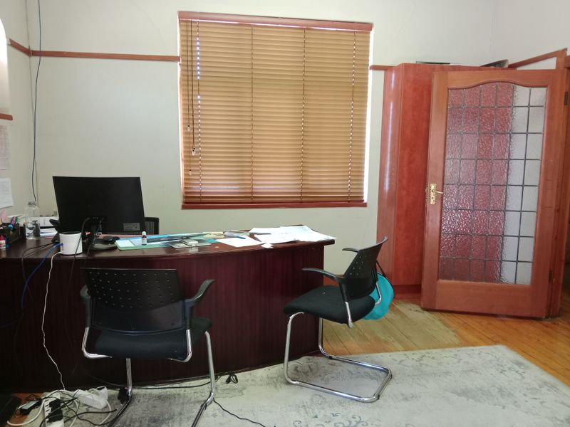 A functional office space featuring timber flooring, a classic timber door with glass inserts, and a window fitted with venetian blinds.