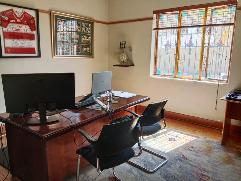 A functional office space featuring a large window with decorative stained glass inserts, security bars, and classic timber picture rail detailing.