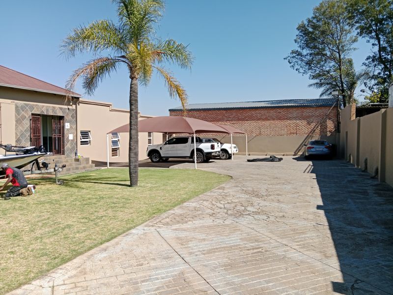 Spacious rear exterior area featuring a paved driveway, shade cloth carport, and landscaped lawn, providing ample parking and outdoor space.