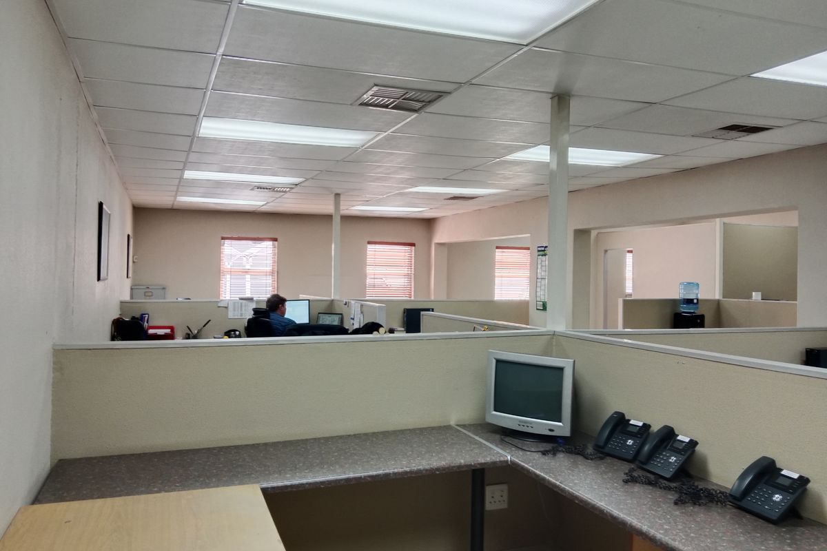 Open-plan office space featuring built-in partitions, laminate work surfaces, and a suspended ceiling with recessed lighting.
