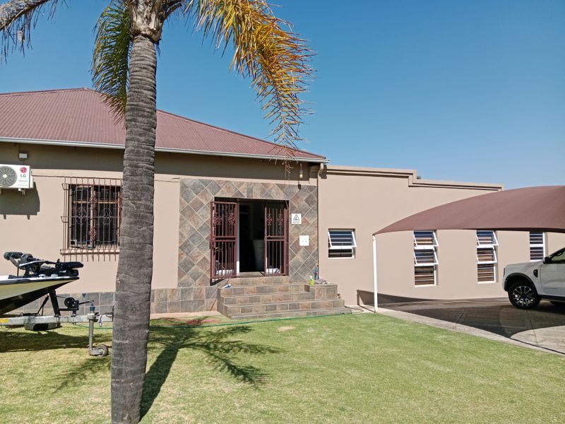 Rear exterior view of the property featuring a tiled entrance, security fixtures, metal roofing, and a covered parking area with a shade sail.