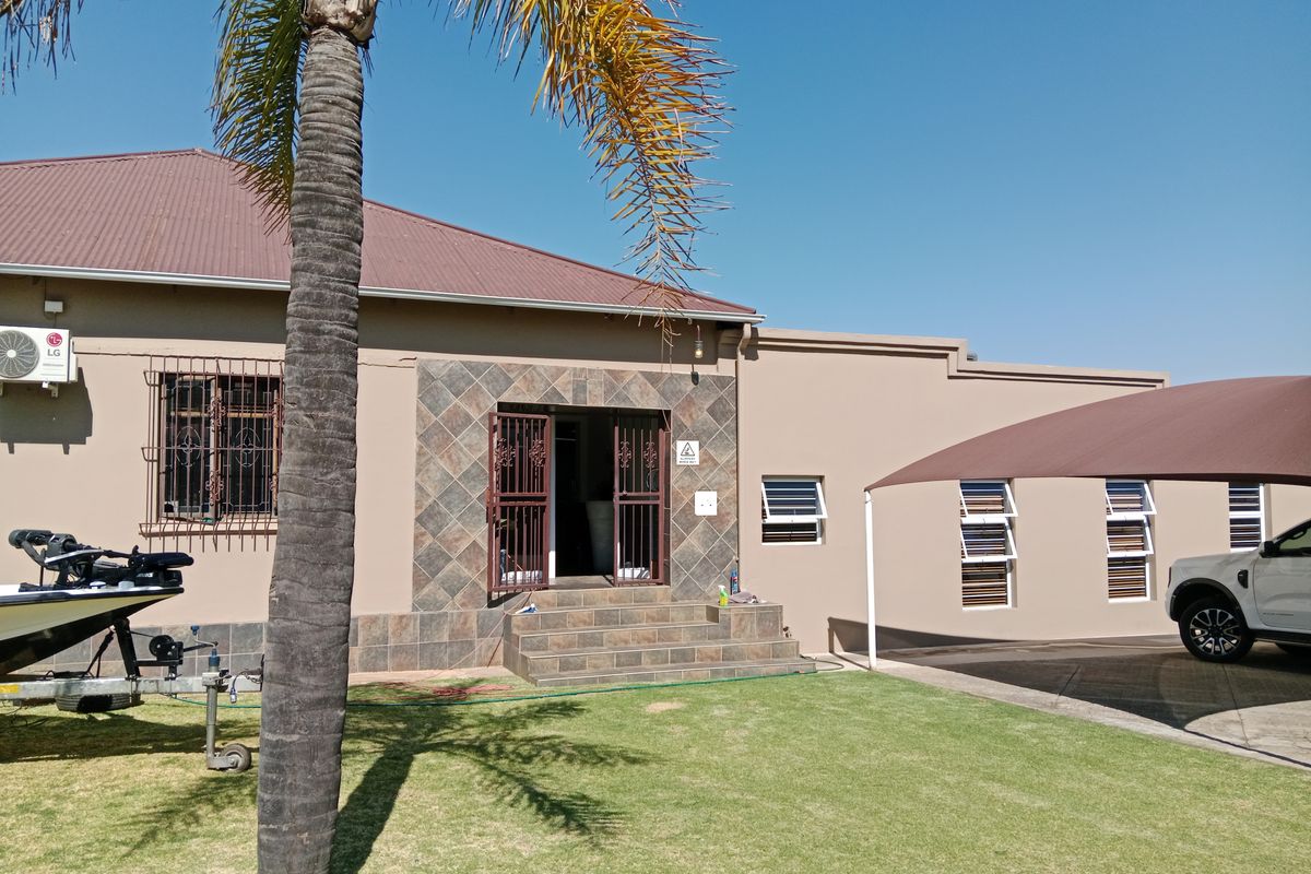 Rear exterior view of the property featuring a tiled entrance, security fixtures, metal roofing, and a covered parking area with a shade sail.