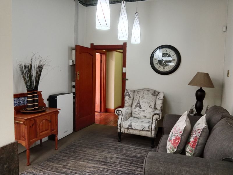 A cozy living room featuring hardwood flooring, decorative ceiling cornices, and warm pendant lighting, leading through a timber door frame to an adjacent space.