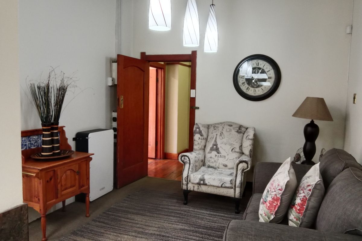 A cozy living room featuring hardwood flooring, decorative ceiling cornices, and warm pendant lighting, leading through a timber door frame to an adjacent space.