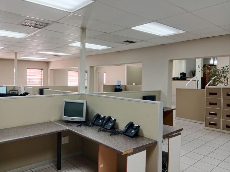 Open-plan office space featuring built-in cubicle workstations, suspended ceilings with recessed lighting, and ceramic tiled flooring throughout.