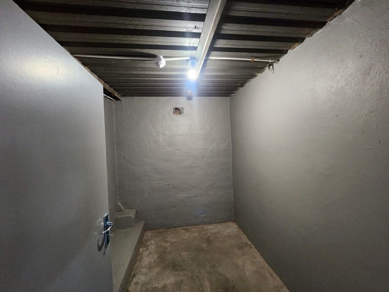 A functional, empty utility space featuring painted masonry walls, a concrete floor, and an exposed corrugated metal ceiling with basic lighting.