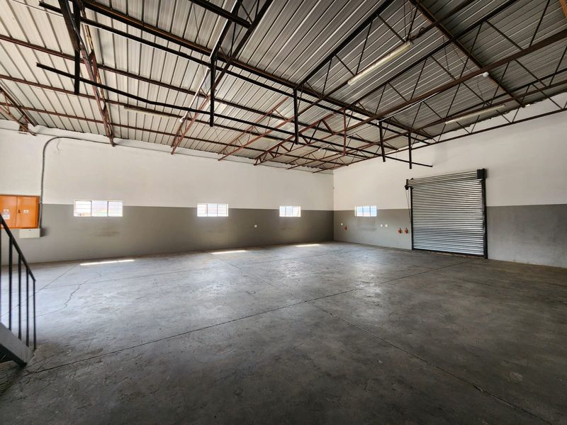 Spacious industrial warehouse unit featuring high exposed steel roof trusses, concrete flooring, and a large roller shutter door for easy access.