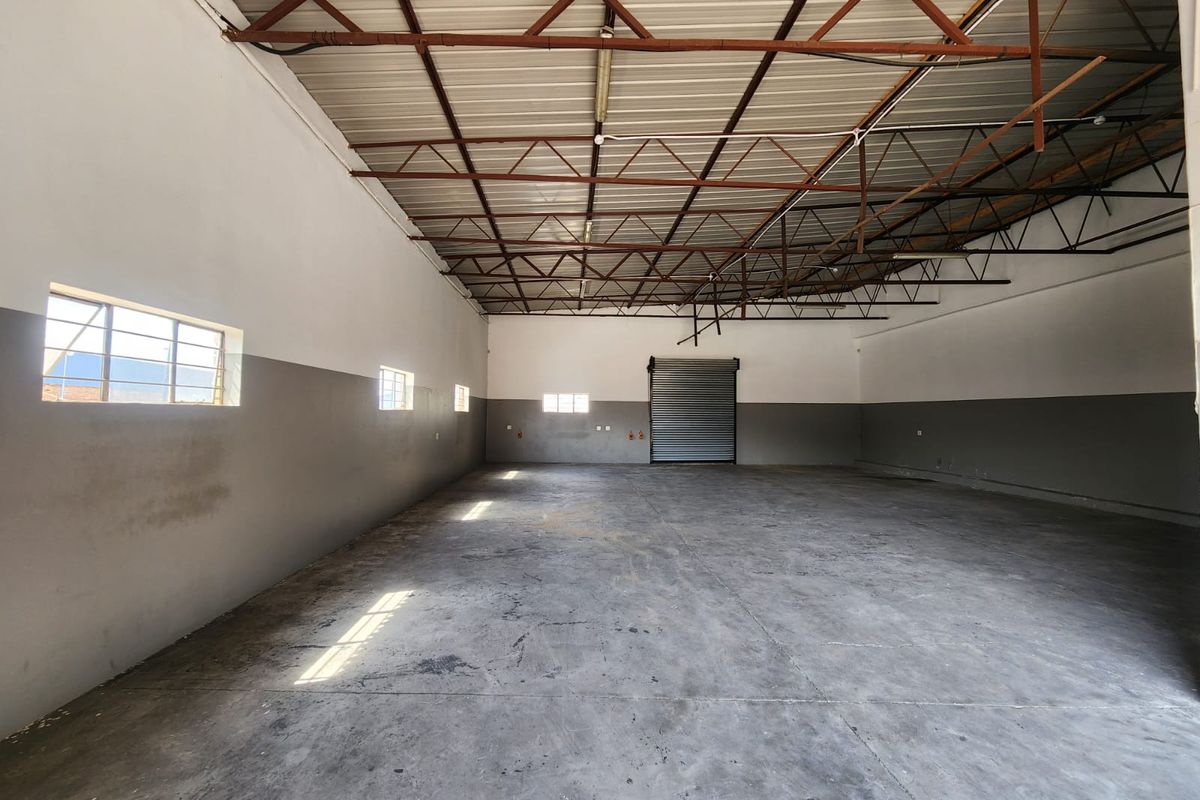 Spacious industrial warehouse unit featuring high exposed steel roof trusses, durable concrete flooring, and a large metal roller shutter door for easy access.