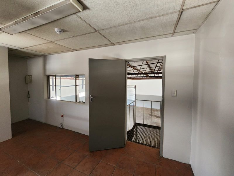 An empty industrial utility space featuring tiled flooring, a suspended ceiling, and direct access to a metal staircase leading to the warehouse floor.