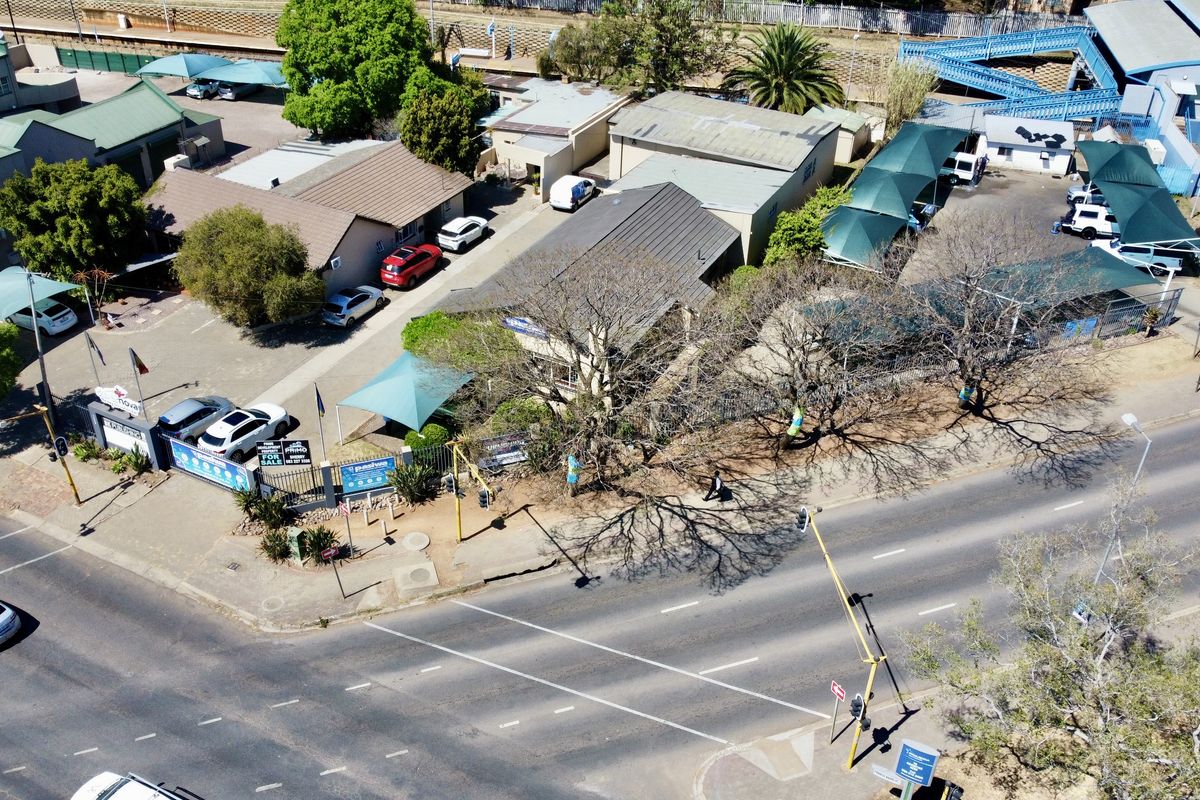 Aerial view of a commercial office property featuring multiple buildings, paved parking areas with shade cloth carports, and perimeter security fencing.