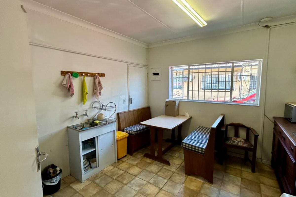 A functional kitchen area featuring tiled flooring, a compact sink unit, and security bars on the window, offering a practical space for office staff.