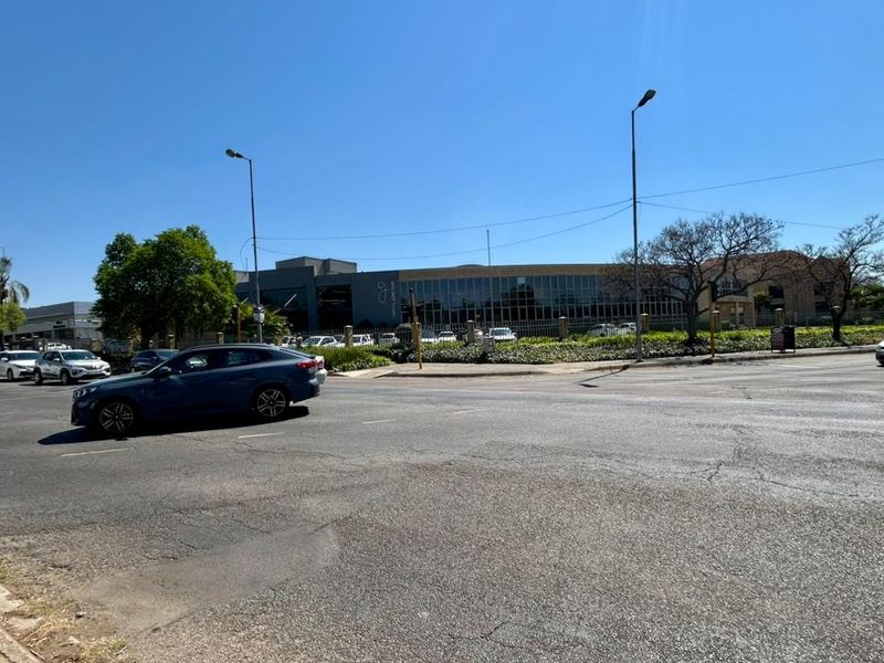 A street-level view of the office property facade, showing the building exterior, perimeter fencing, and surrounding road infrastructure.