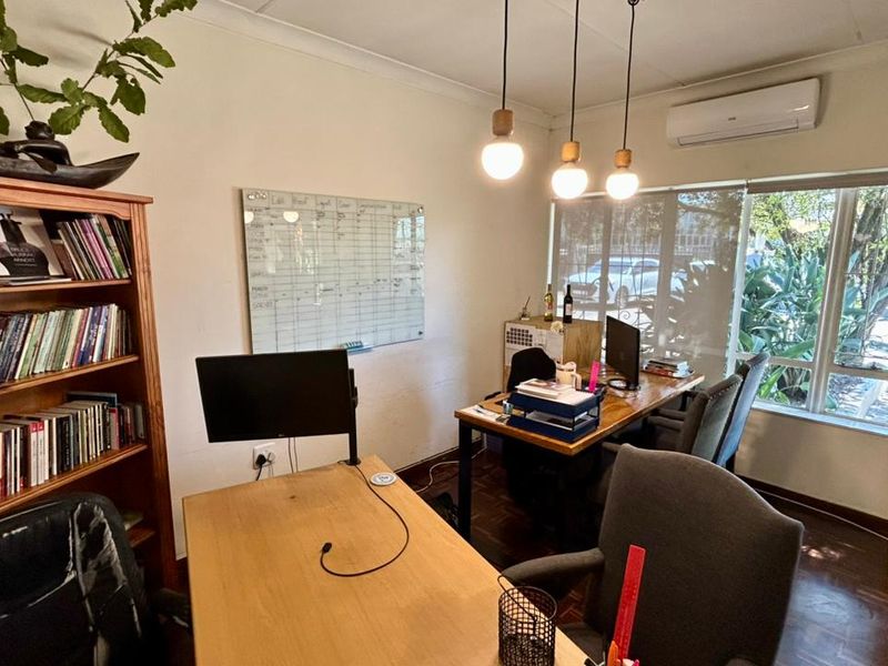 A functional office space featuring timber flooring, split-system air conditioning, pendant lighting, and a large window providing natural light.