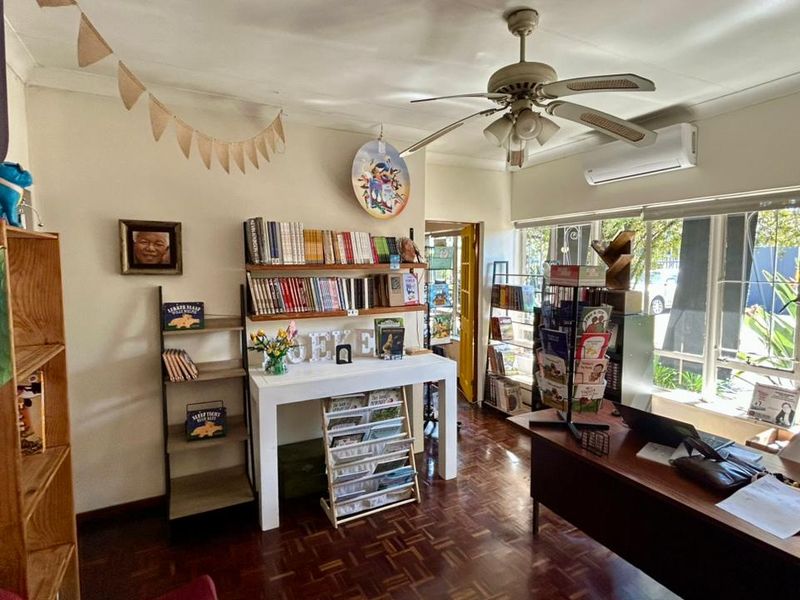 A functional office space featuring parquet flooring, a ceiling fan, and a wall-mounted air conditioning unit with large windows providing natural light.