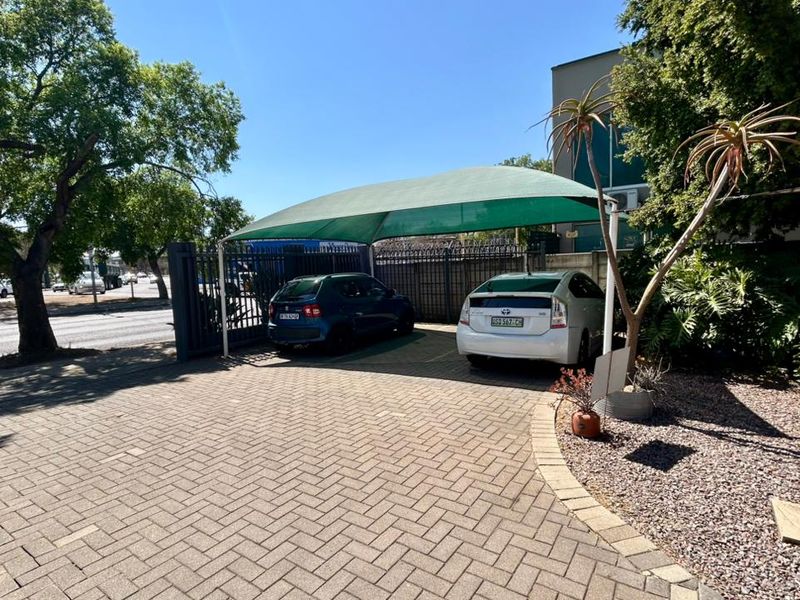 Exterior view of the office property featuring a paved driveway, secure metal gate, and a shaded parking area.