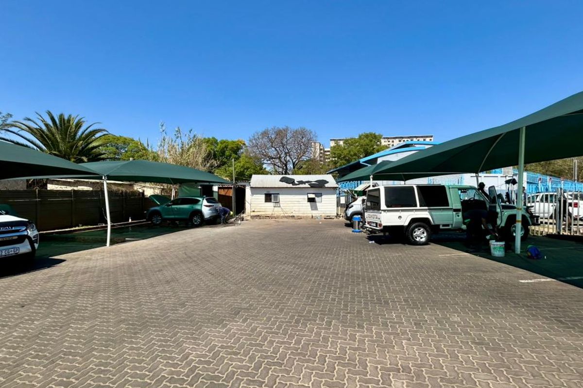 Exterior view of a paved parking area featuring multiple shade cloth carports and a small utility structure at the rear.