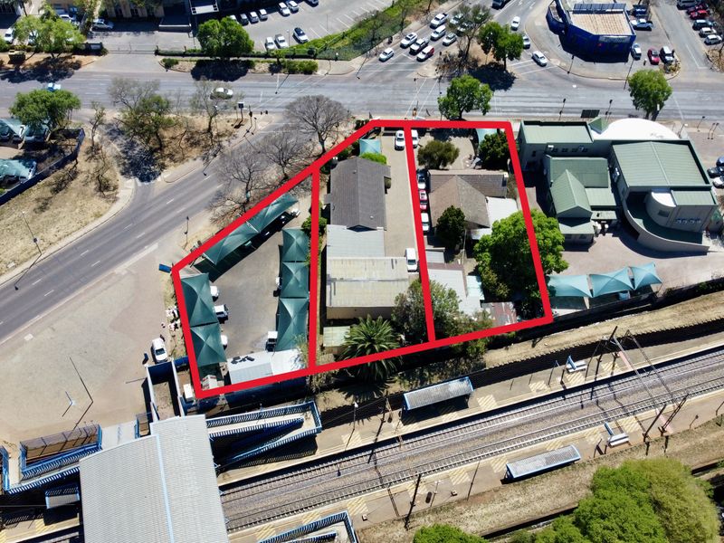Aerial view of an office property featuring multiple buildings, extensive paved parking areas, and shade cloth carports adjacent to a railway station.