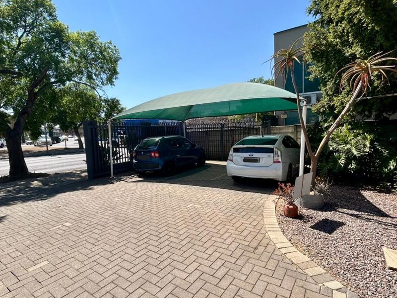 Front exterior view of the office property featuring a paved driveway, secure metal gate, and a shaded parking area.