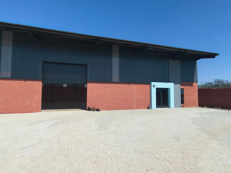 Modern industrial warehouse facility featuring a large roller shutter door, brick and metal facade, and a spacious paved yard area.