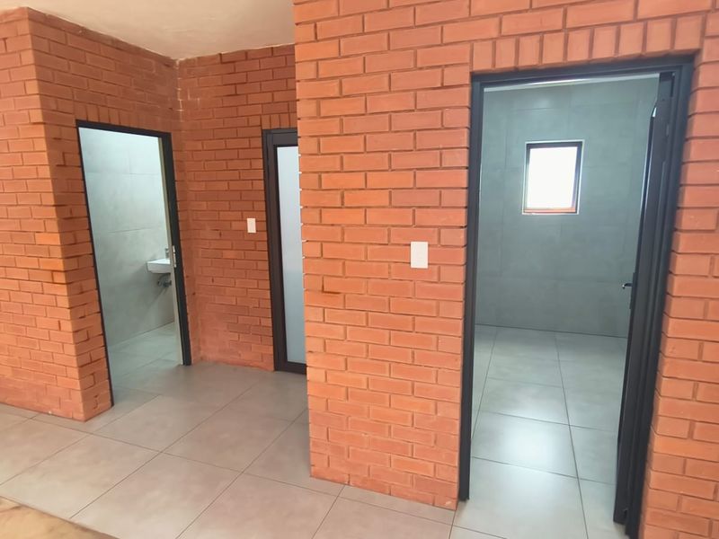 A clean hallway featuring exposed brick walls and tiled flooring, providing access to multiple internal rooms with modern finishes.