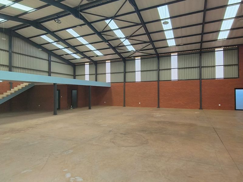 Spacious industrial warehouse unit featuring high ceilings with exposed steel trusses, translucent roof panels, concrete flooring, and a mezzanine level with staircase access.