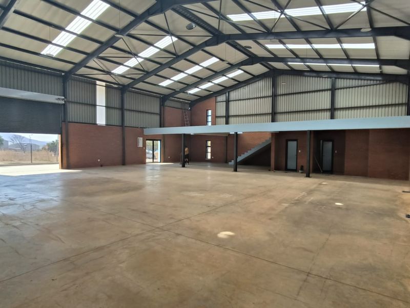Spacious industrial warehouse featuring exposed steel portal framing, high ceilings with skylights, concrete flooring, a roller shutter door, and an integrated mezzanine level.