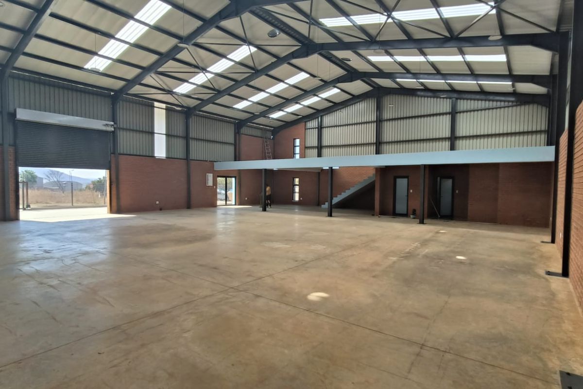 Spacious industrial warehouse featuring exposed steel portal framing, high ceilings with skylights, concrete flooring, a roller shutter door, and an integrated mezzanine level.