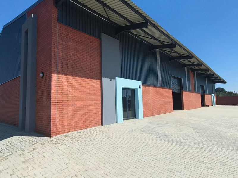 Modern industrial warehouse facility featuring a brick and metal facade, roller shutter doors, and an expansive paved yard area.