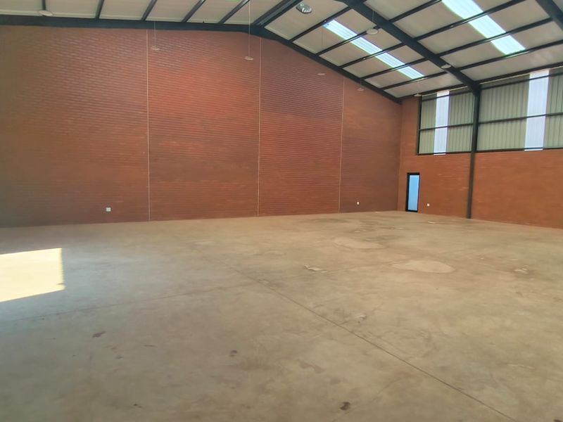 Spacious industrial warehouse unit featuring exposed brick walls, durable concrete flooring, high steel portal frame ceilings, and natural light from integrated skylights.