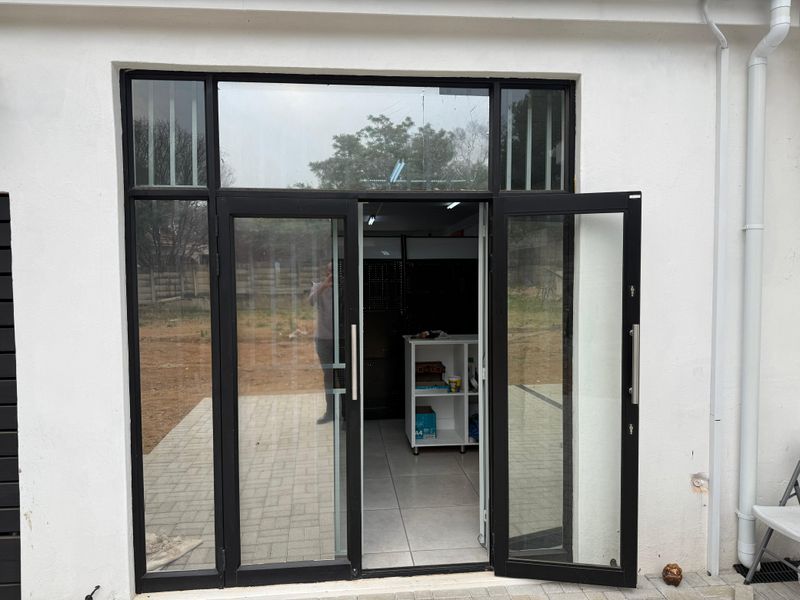 Exterior view of a retail entrance featuring modern black aluminium-framed glass double doors with a transom window and paved threshold.