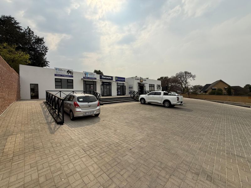 Front exterior view of a commercial retail property featuring a paved parking area, multiple storefront entrances, and secure boundary walling.