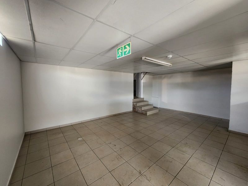 An empty industrial utility space featuring tiled flooring, a suspended ceiling, and an internal staircase leading to an upper level.