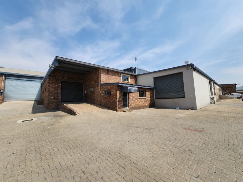 Industrial property exterior featuring a brick facade, multiple roller shutter doors, a loading ramp, and a spacious paved yard area.
