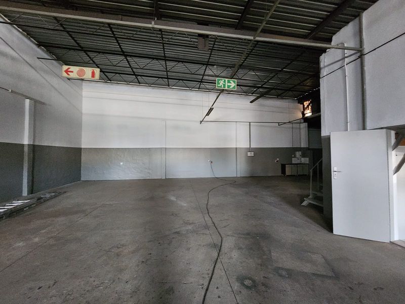 Spacious industrial utility area featuring high exposed ceilings, durable concrete flooring, and essential safety signage, suitable for various commercial or storage applications.