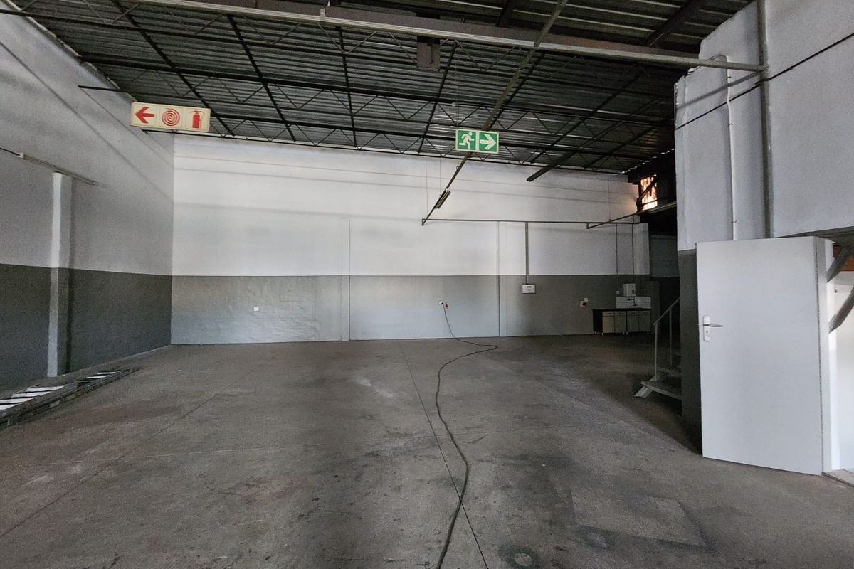 Spacious industrial utility area featuring high exposed ceilings, durable concrete flooring, and essential safety signage, suitable for various commercial or storage applications.