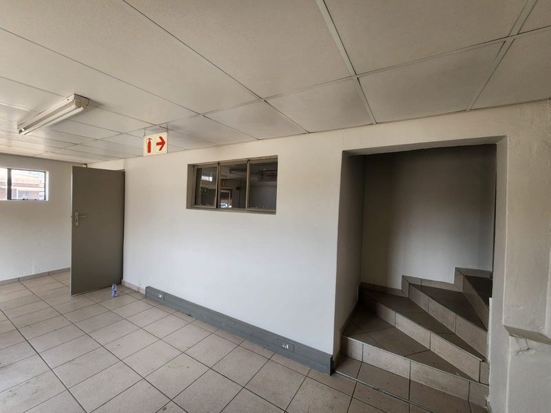 A functional industrial hallway featuring tiled flooring, a suspended ceiling, internal window, and a staircase leading to another level.