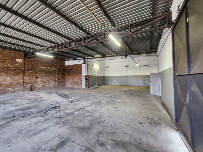 Spacious industrial warehouse unit featuring exposed brickwork, high-clearance steel truss roofing, concrete flooring, and a large sliding access door.