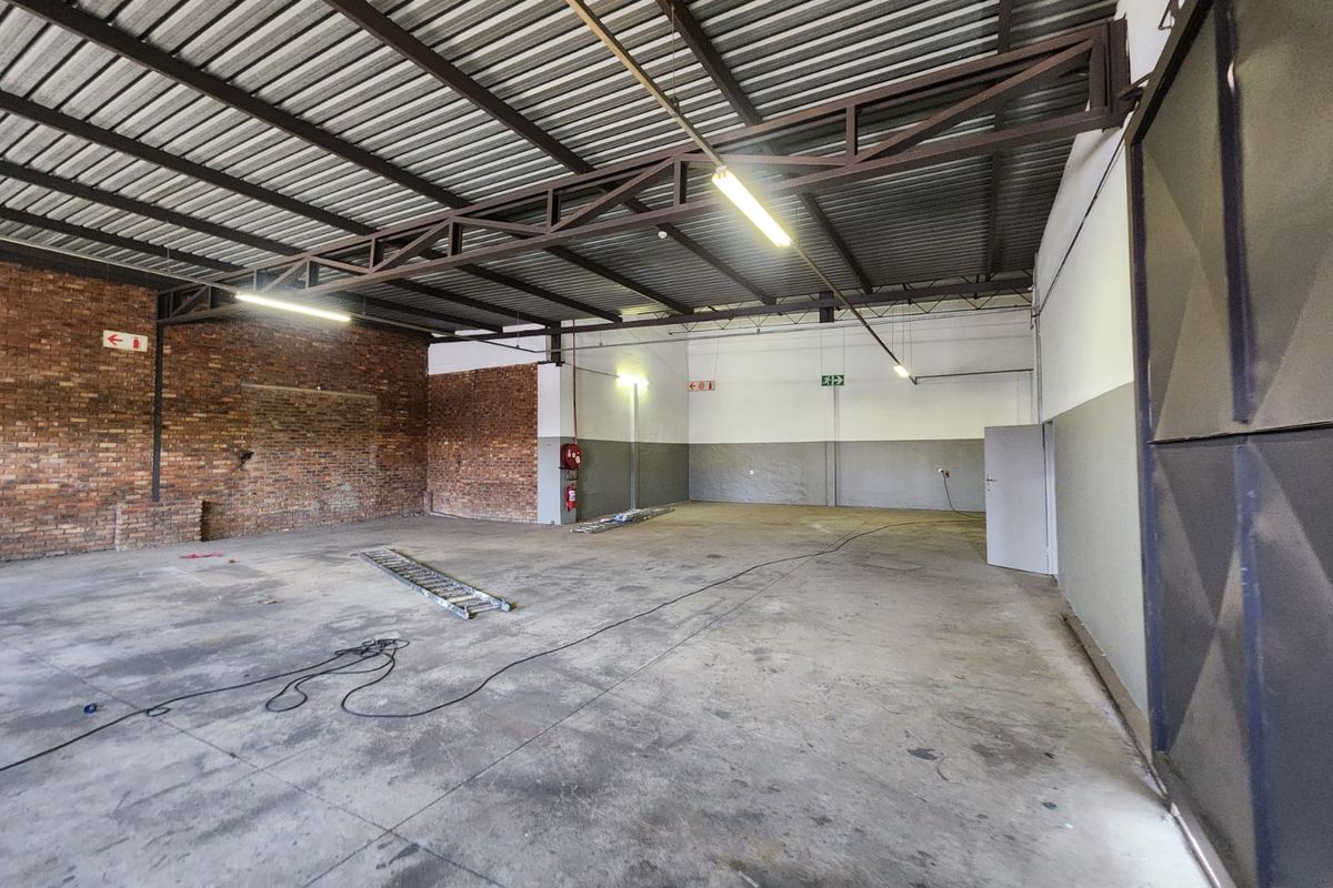 Spacious industrial warehouse unit featuring exposed brickwork, high-clearance steel truss roofing, concrete flooring, and a large sliding access door.