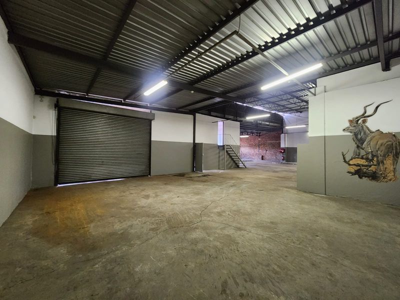 Spacious industrial utility area featuring high ceilings with exposed steel trusses, concrete flooring, and a large roller shutter door for easy access.