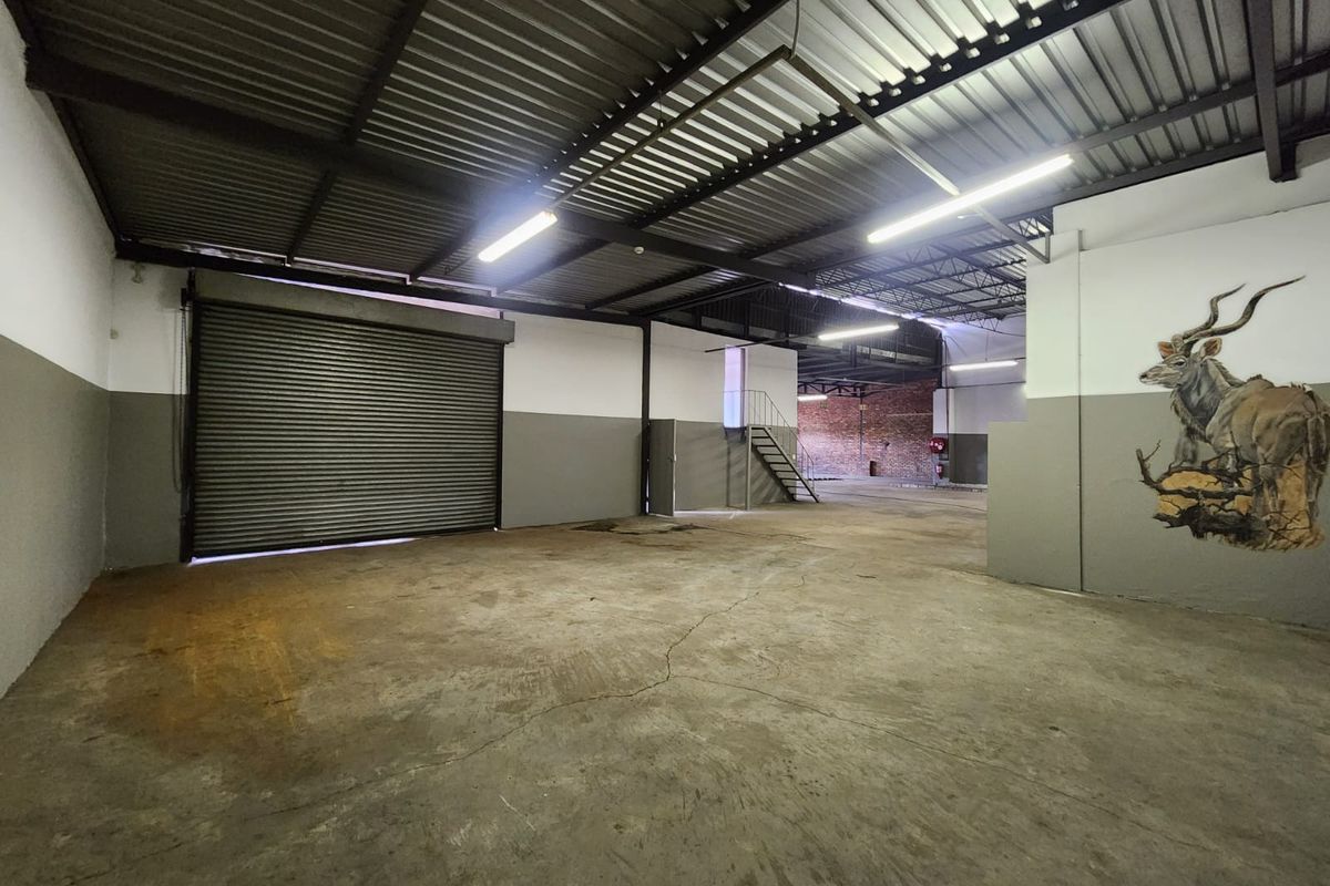 Spacious industrial utility area featuring high ceilings with exposed steel trusses, concrete flooring, and a large roller shutter door for easy access.