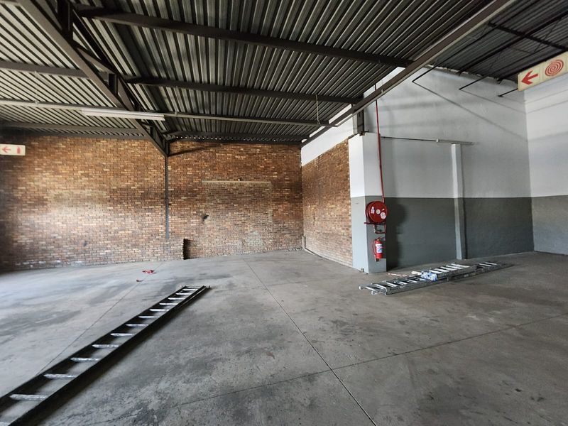 Spacious industrial utility area featuring exposed brick walls, concrete flooring, and high-clearance steel roof trusses with integrated fire safety equipment.