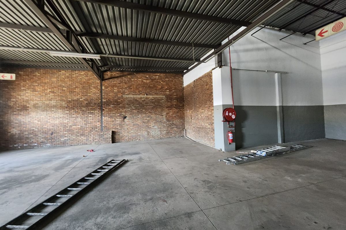 Spacious industrial utility area featuring exposed brick walls, concrete flooring, and high-clearance steel roof trusses with integrated fire safety equipment.