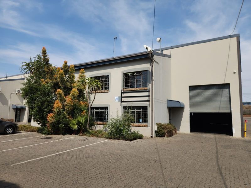 Front elevation of an industrial property featuring a large roller shutter door, paved parking area, and secure steel-framed windows.