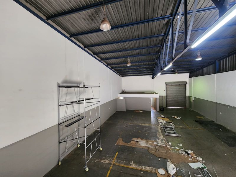 Spacious industrial warehouse unit featuring high exposed steel roof trusses, a roller shutter door, and a mezzanine level, suitable for storage or workshop use.