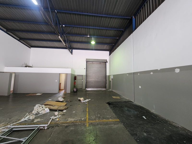 Spacious industrial warehouse unit featuring high ceilings with exposed steel trusses, a large roller shutter door, and durable concrete flooring.